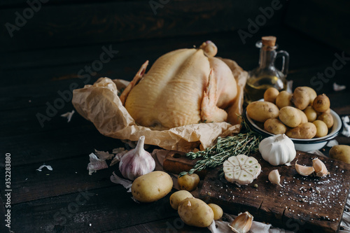Raw whole farm chicken with potatoes, garlic, thyme and spices. Healthy, nutrition. Dark wood background