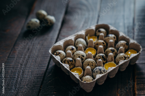 Quail eggs in craft paper box on dark wooden background, Part of the eggs is broken, visible yolk. farm products, organic products, Healthy food concept