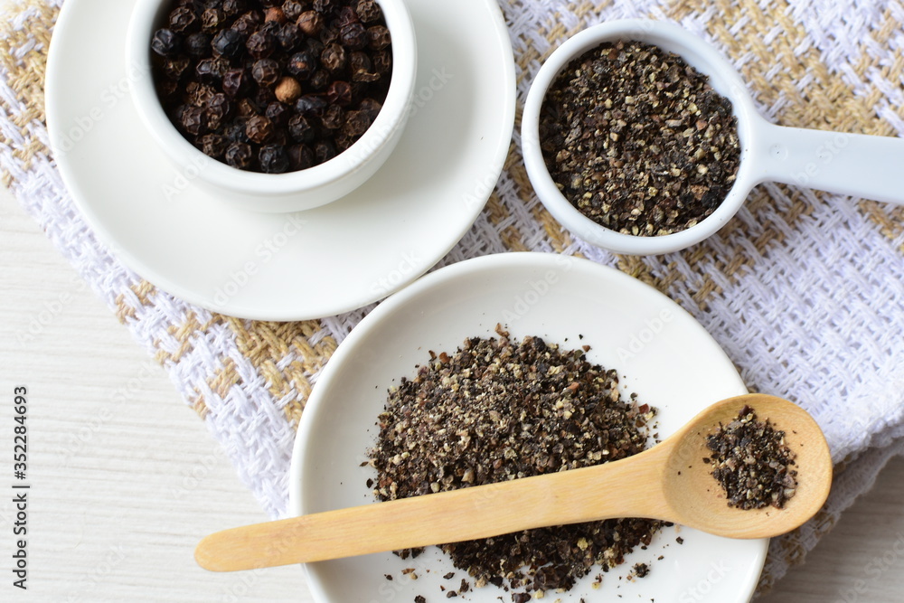 Whole and ground black peppercorns on white wooden background Whole and ground black peppercorns on white wooden background