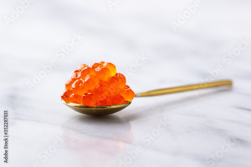 Red salmon caviar in golden spoon. Marble background. Close up.
