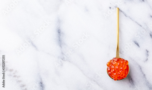 Red salmon caviar in golden spoon. Marble background. Copy space. Top view.