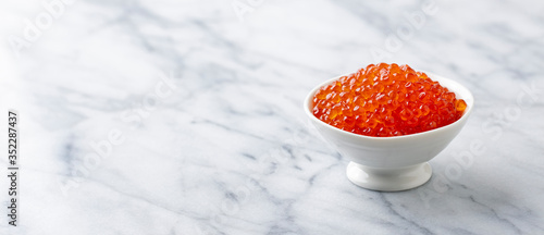 Red salmon caviar in white bowl. Marble background. Copy space.