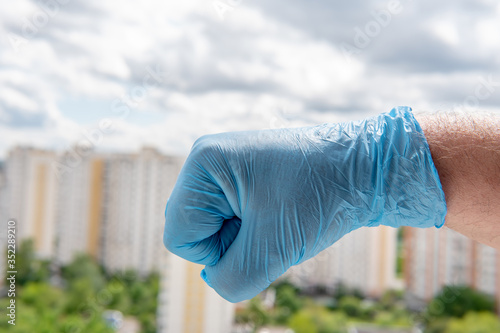 Quadro em tela A male hand in a medical glove clenched into a fist against a cityscape