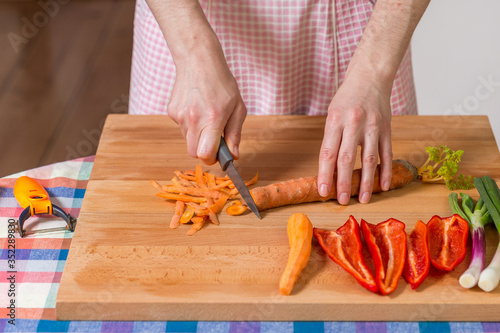 Close up of hands peeling and cutting carrots on a wooden board...Healthy food preparation concept