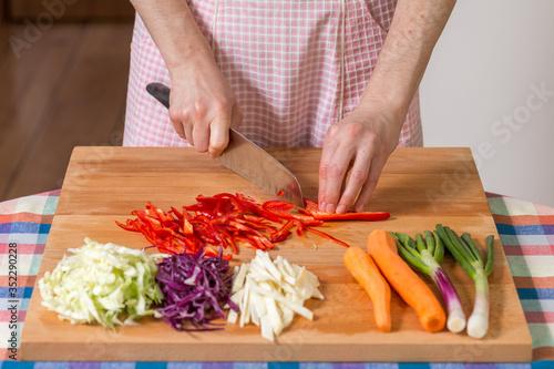 Close up of hands chopping red peppers on a wooden board. Healthy food preparation concept