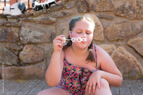Portrait of Obese blonde teenager with braids in her hair making soap bubbles. Concept of children playing and having fun.