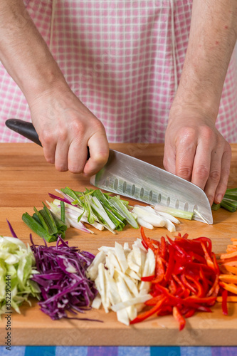 Close up of hands chopping scallions on a wooden board. Healthy food preparation concept
