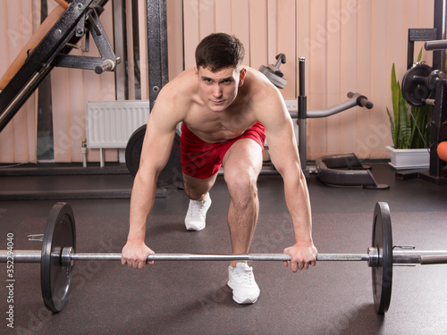 Young man flexing muscles with barbell in gym.