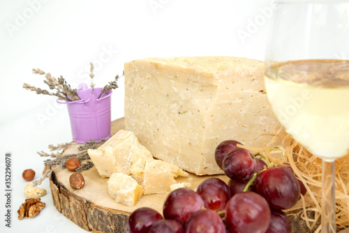 goat aged hard cheese slices with the addition of lavender decorated with grapes wine, nuts and lavender, lies on a wooden plate, close-up, white background, photo with cheese 
visible cheese texture