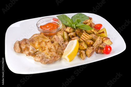 Gourmet chicken steak with potatoes and tomatoes salsa on a white plate, isolated on black background.