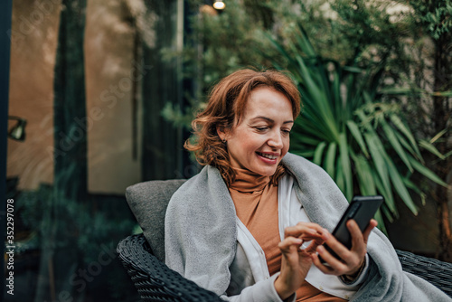 Close-up portrait of a cheerful woman using smart phone in home garden.