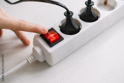 A woman turns on an electric surge protector. Protection of household appliances from electrical interference. Home safety, close up.