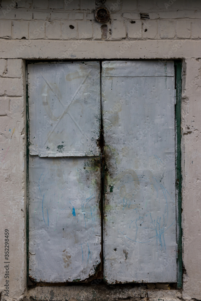 Old metal and wood door painted with white-blue paint against the background of an old white tiles
