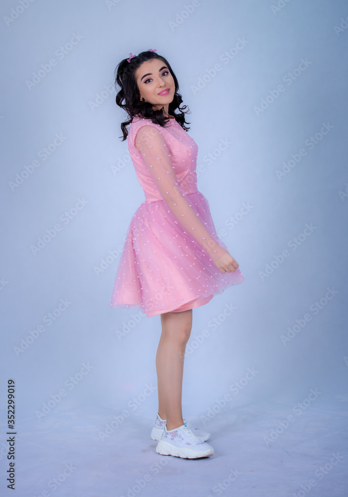 Portrait Of Beautiful Young girle Standing Against blue Background,girl in a pink dress,Happy cheery smiling young cute girl posing isolated,White running shoes Portrait Of Beautiful Young girle Standing Against blue Background,girl in a pink dress,Happy cheery smiling young cute girl posing isolated,White running shoes