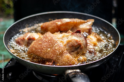 A close-up shot of streaky pork cooking in a frying pan has hot oil and it looks delicious.