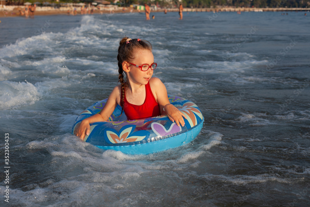 Obraz premium young girl in glasses plays in the water on an inflatable donut in a hot sunny summer