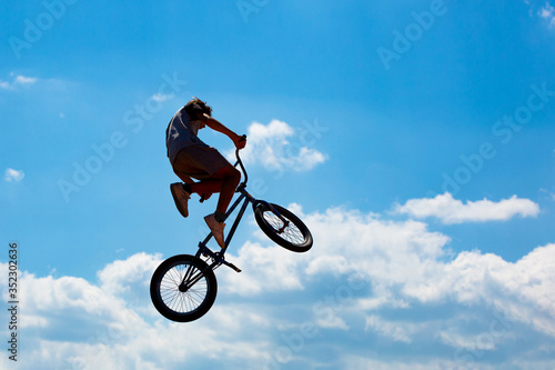 Silhouette of a man jumping on a Bicycle against a blue sky with white clouds.