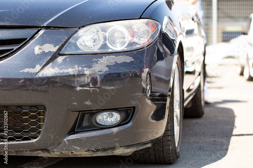 Black car, close-up of a scratched bumper and headlight.