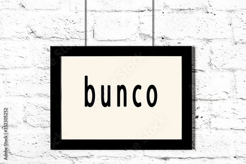 Black frame hanging on white brick wall with inscription bunco photo