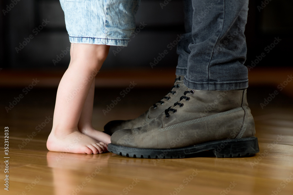 A little girl with bare feet is standing in front of her father in the hallway