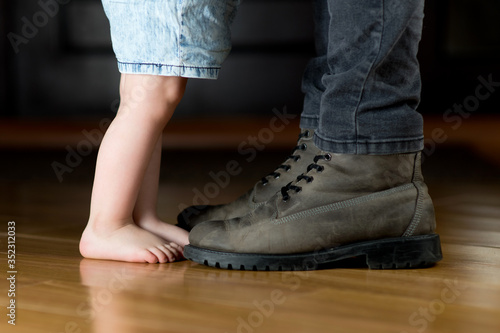 A little girl with bare feet is standing in front of her father in the hallway