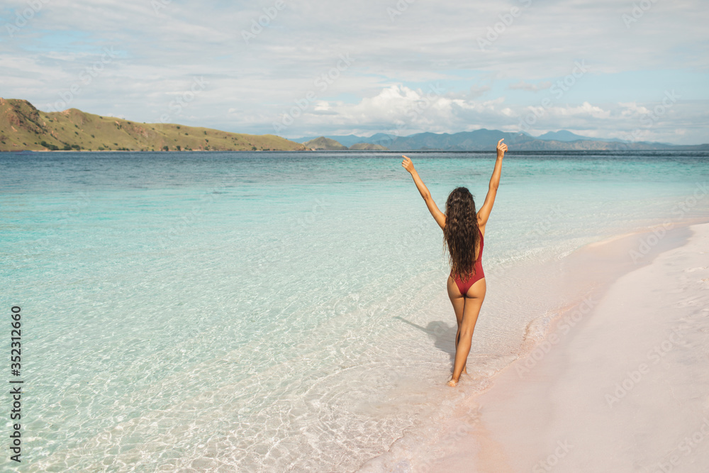 Woman in red swimsuit walking by amazing paradise tropical beach with nobody around. Summer concept. View from behind. Empty place for sign. Woman in red swimsuit walking by amazing paradise tropical beach with nobody around. Summer concept. View from behind. Empty place for sign.