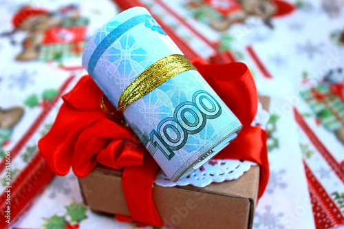 Money roll Russian banknote 1000 one thousand rubles and a gift box with a red ribbon bow, as a present for New Year and Christmas.