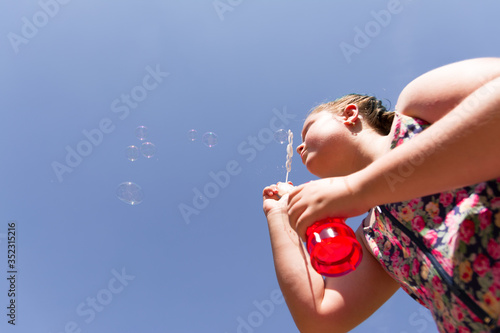 Chubby blonde teenager with braids in her hair making soap bubbles. Concept children playing