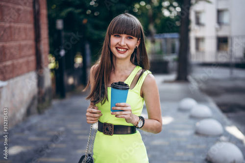 Pretty brunette girl in green dress with cup of coffee walking outdoor on the street © bedya