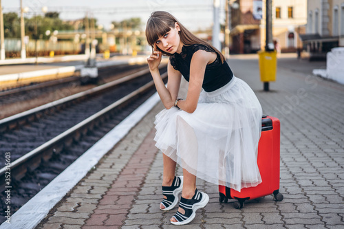 Female traveler with red suitcase waiting train on railway station