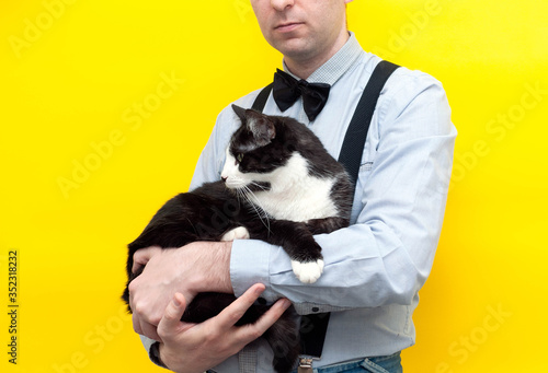 cropped view of man in blue shirt with long sleeves holding on arms cute black and white taxedo cat on yellow background