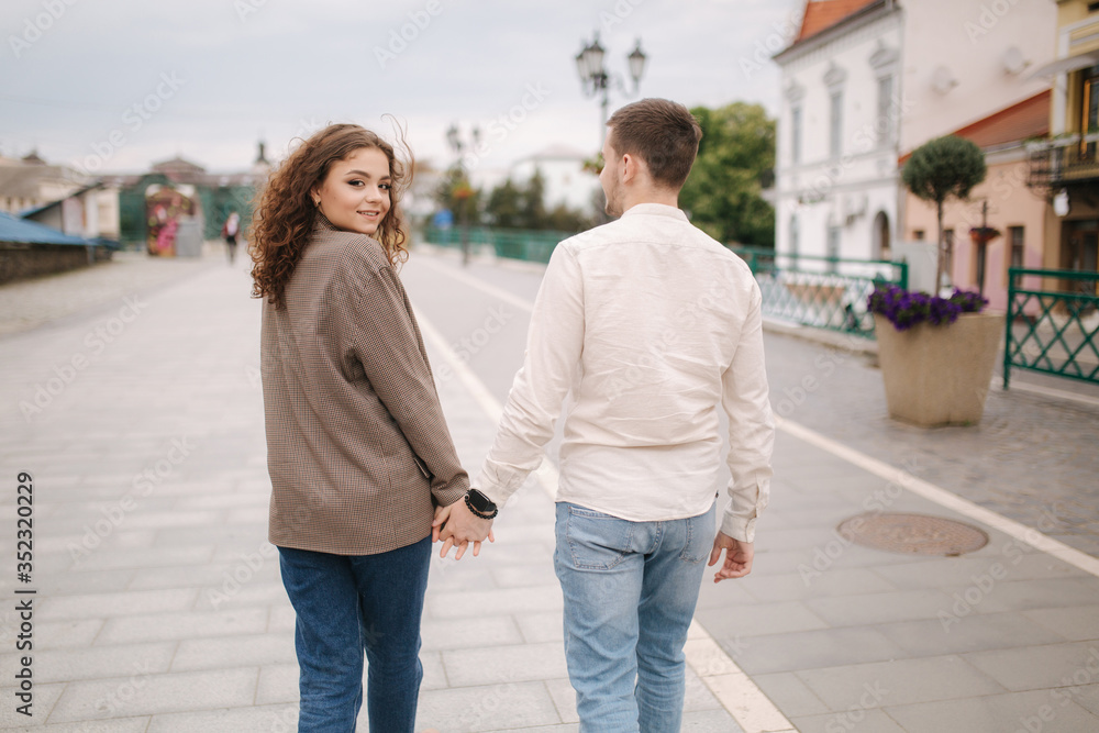 Back view of Happy couple walking in the city. Attractive young woman and handsome young man in centre of the city. Smiled people Back view of Happy couple walking in the city. Attractive young woman and handsome young man in centre of the city. Smiled people