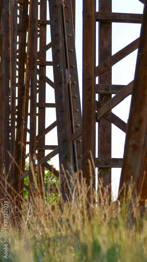 An old disused rusted brown bridge in the countryside connecting two banks across a river, formerly used for busy agricultural traffic An old disused rusted brown bridge in the countryside connecting two banks across a river, formerly used for busy agricultural traffic