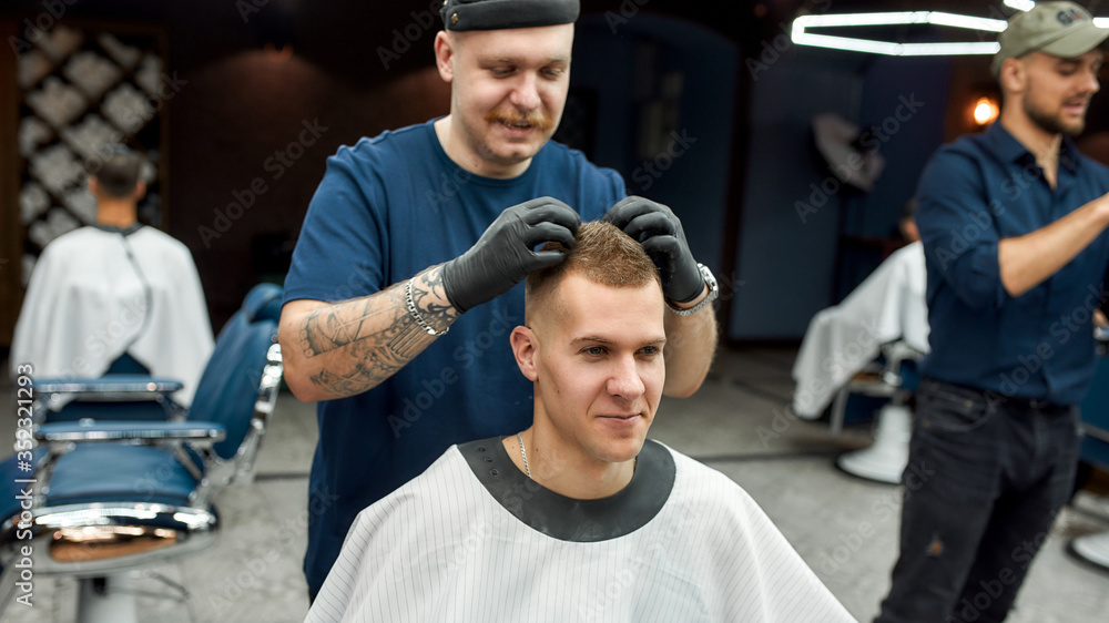 Great job. Stylish barber with tattoo on hand making hair styling for young handsome guy sitting in barber shop chair. Barbershop concept. Getting haircut Great job. Stylish barber with tattoo on hand making hair styling for young handsome guy sitting in barber shop chair. Barbershop concept. Getting haircut
