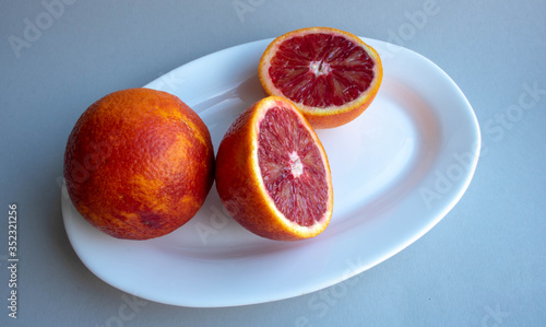 Group of three whole fresh orange mandarine on white ceramic plate isolated on gray background