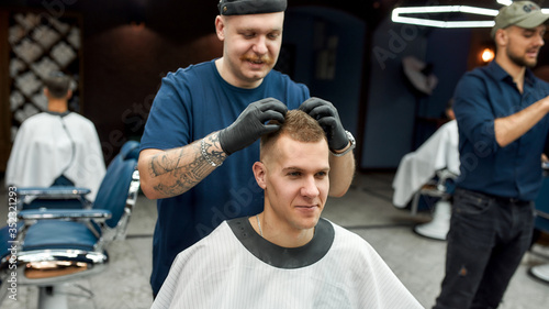 Great job. Stylish barber with tattoo on hand making hair styling for young handsome guy sitting in barber shop chair. Barbershop concept. Getting haircut