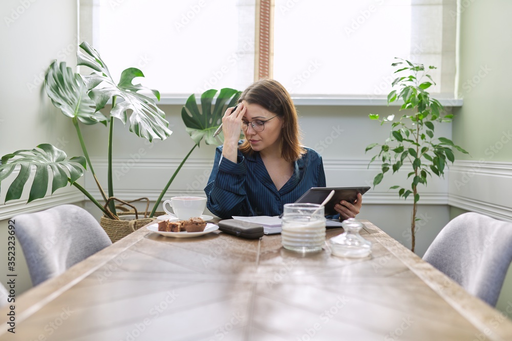 Serious mature woman working at home, using digital tablet, business notebook Serious mature woman working at home, using digital tablet, business notebook