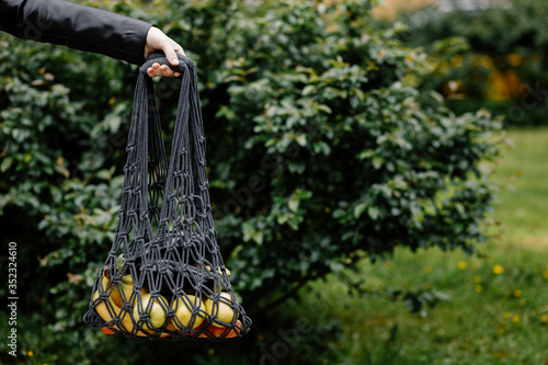 Mesh bag with fruits, vegetables in female hand. Hand of stylish young woman hold string net shopping bag. Modern reusable shopping, eco lifestyle, zero waste concept. Healthy, organic, clean eating.