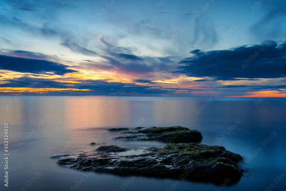Boulders in smooth ocean with sunset background, long exposure