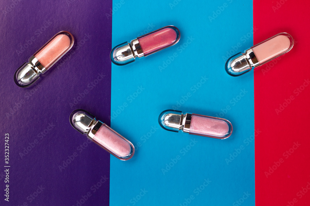 Lip glosses are arranged in a chaotic manner on a colorful background. Cosmetical tools Lip glosses are arranged in a chaotic manner on a colorful background. Cosmetical tools