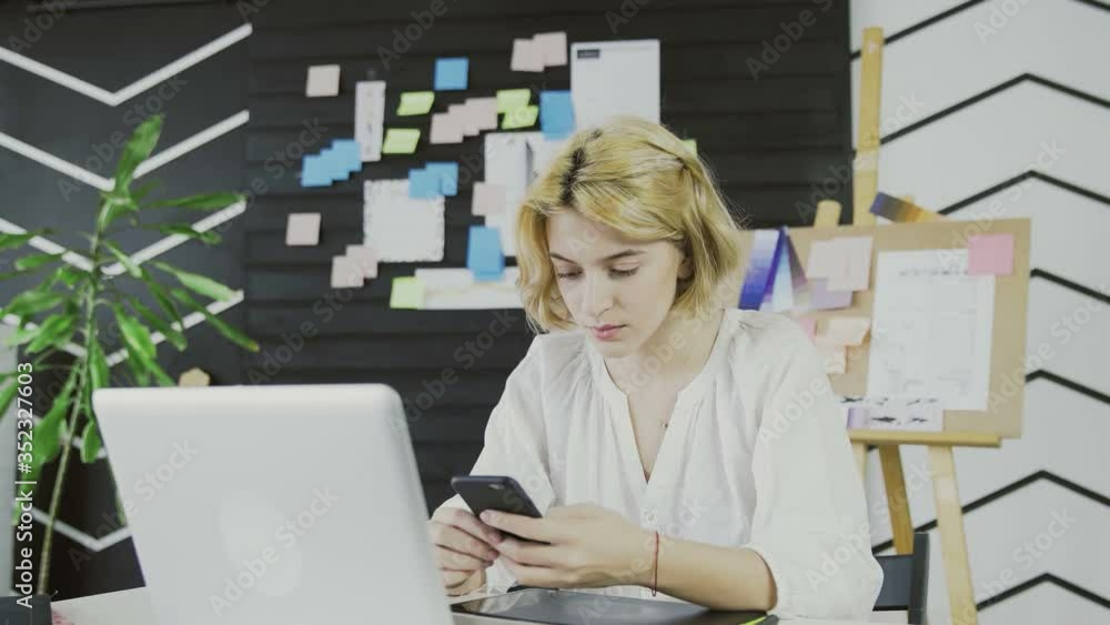 Attractive female designer using smart phone in the office. Attractive female designer using smart phone in the office.