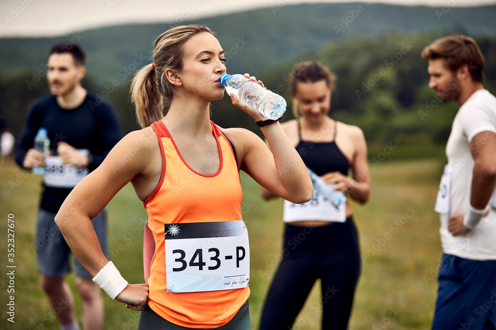 Obraz premium Thirsty athletic woman drinking water after running a marathon in nature.