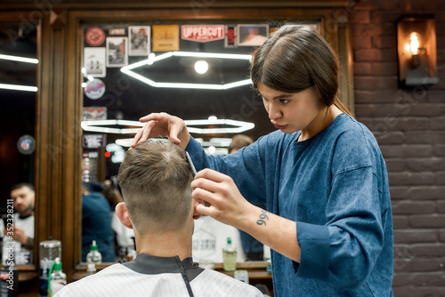 Cool hairstyle. Young caucasian man getting new haircut in the modern barbershop. Professional barber girl doing haircut for her client. Beauty salon