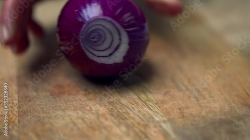 A close-up look of a rolling red onion on the kitchen table and a woman's hand taking/grabbing the red onion and placing it on a cutting board