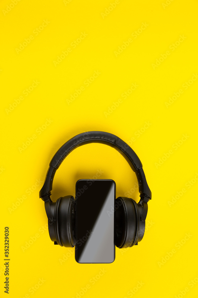 Black wireless headphones and smartpnone on bright yellow vertical colorful background with copy space Black wireless headphones and smartpnone on bright yellow vertical colorful background with copy space