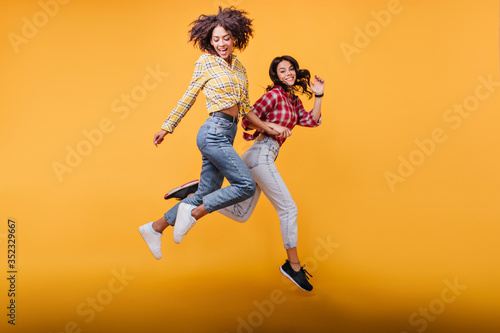 Young women with curly hair run on orange background. Models in streetwear posing in jump