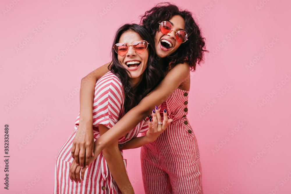 African sisters with dark curls are having fun in wonderful mood. Portrait of embracing girls with beautiful appearance - obrazy, fototapety, plakaty 