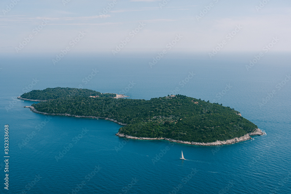 Lokrum is a small island in the Adriatic Sea, near Dubrovnik, Croatia. A small sailing yacht is sailing next to the island.