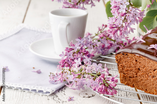 Brownie, watered with chocolate on a wooden background with a bouquet of lilacs