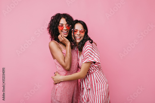 Cousins in dark curly hair in great mood posing for portrait. Girls in pink outfits have fun